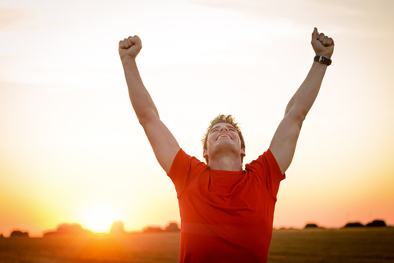 A man in addiction recovery raises his arms in celebration.